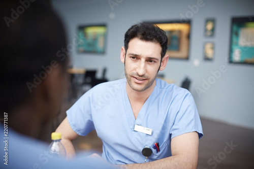 Confident male nurse talking with coworker at hospital cafeteria photo