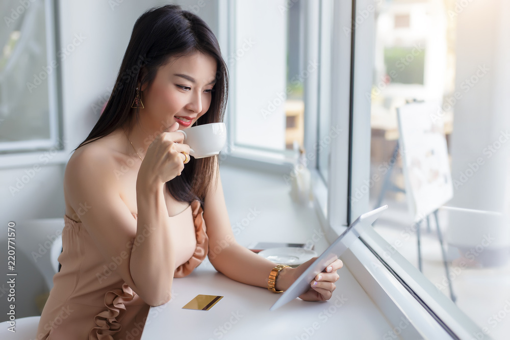 Young asian woman sitting drinking coffee and using tablet at coffee shop.