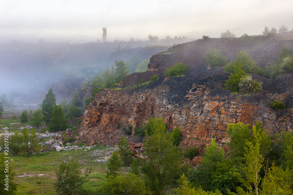 The stony cliff of abandoned sandstone quarry. Foggy early morning