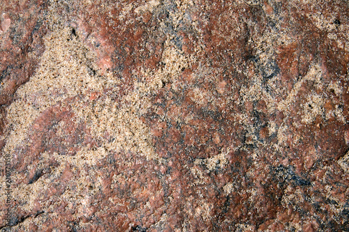 Uneven surface of pink granite boulder partially covered with sand, may be used as background or texture photo