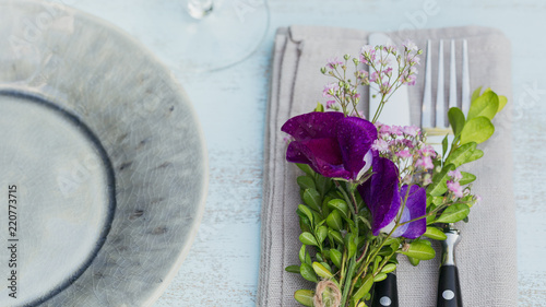 Rustic table setting with purple flowers on light wooden table.