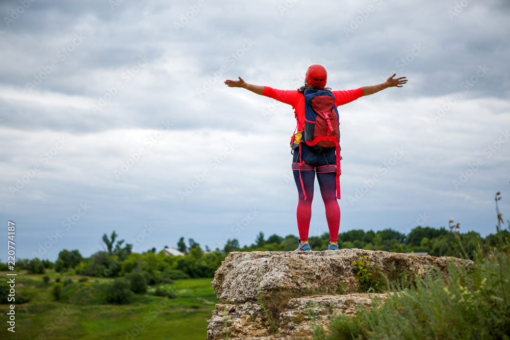 Picture from back of female tourist with arms raised on hill