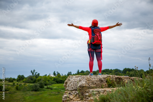 Picture from back of female tourist with arms raised on hill