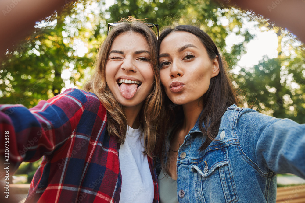 Beautiful ladies students walking in the park take a selfie by mobile phone.