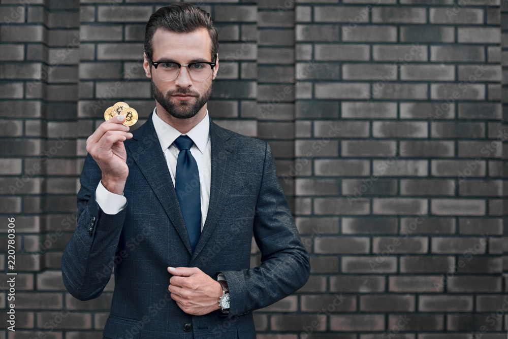 Photo of handsome rich businessman in suit showing golden bitcoin focused on camera Photo of handsome rich businessman in suit showing golden bitcoin focused on camera