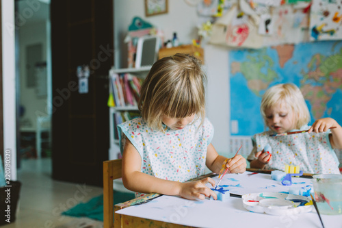 Portrait of happy adorable little girls painting at home together.