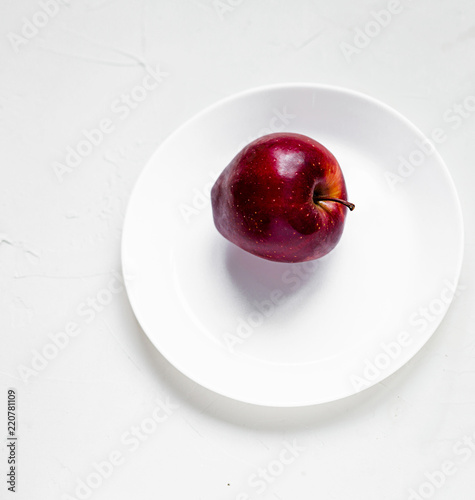 A ripe red apple on a white plate. Top view, copy space