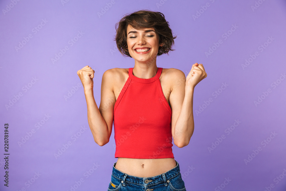 Image closeup of slim brunette woman 20s in casual wear smiling while rejoicing and clenching fists in success, isolated over violet background Image closeup of slim brunette woman 20s in casual wear smiling while rejoicing and clenching fists in success, isolated over violet background