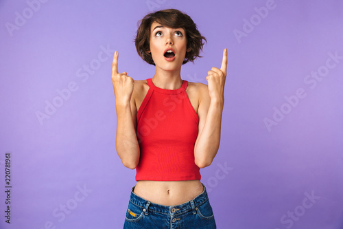Image of excited woman 20s in casual wear pointing fingers upward at copyspace with open mouth, isolated over violet background