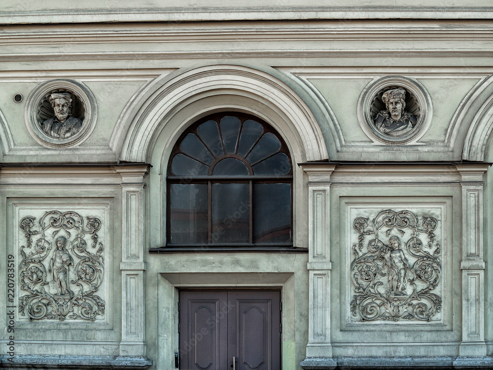 The facade of the building with two bas-reliefs, a sculptural panel, a door and a round stained-glass window in St. Petersburg The facade of the building with two bas-reliefs, a sculptural panel, a door and a round stained-glass window in St. Petersburg