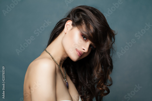 Female face. Woman with long curly hairstyle on blue background, fashion portrait