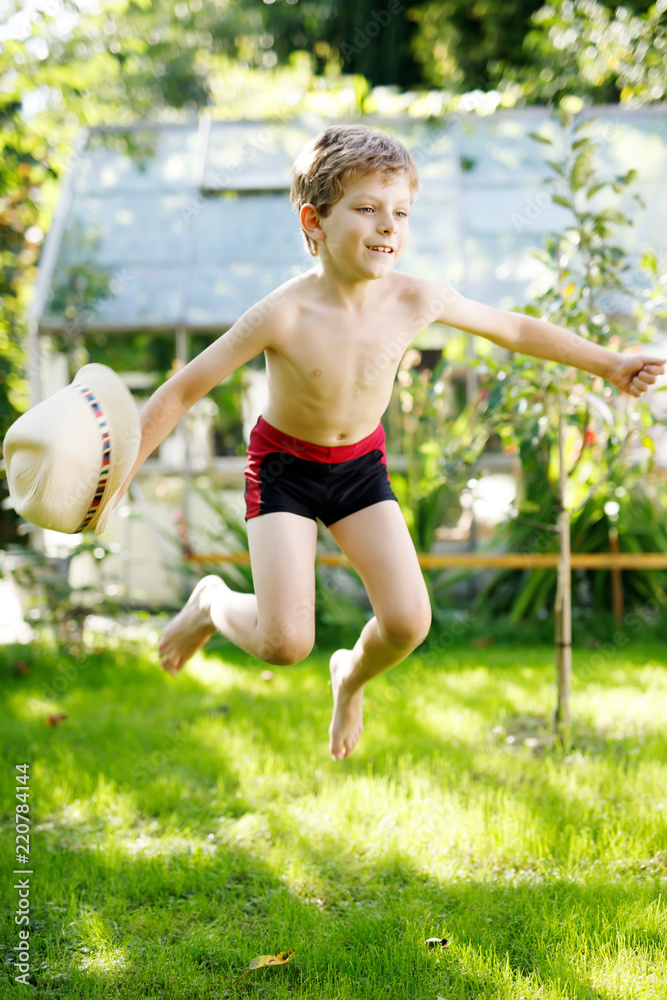 Cute active kid boy jumping in the garden on warm sunny summer day. Happy kid looking at the camera. Adorable child with blond hairs and blue eyes Cute active kid boy jumping in the garden on warm sunny summer day. Happy kid looking at the camera. Adorable child with blond hairs and blue eyes