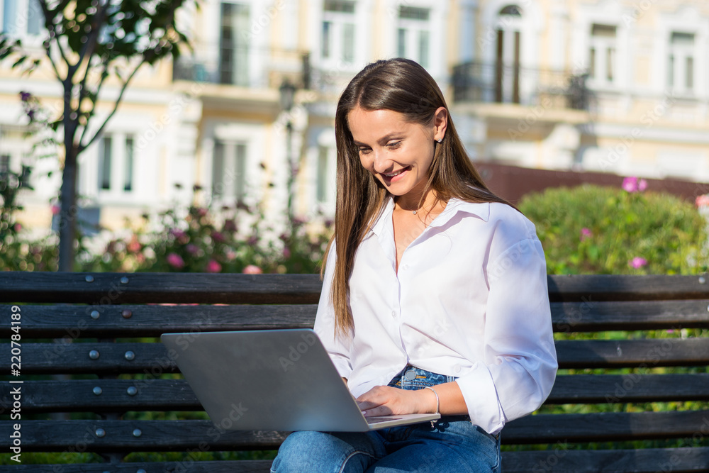Young beautiful female with a laptop sits on a bench in outdoor. Young beautiful female with a laptop sits on a bench in outdoor.