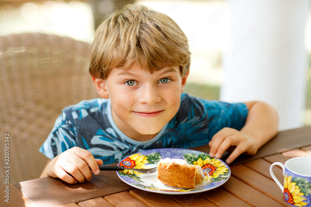 Beautiful kid boy eating apple pie in restaurant on vacations. Happy healthy child in an outdoor cafe in summer time, eating cake