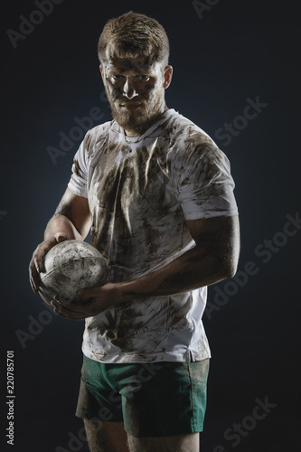 Isolated dirty rugby player with rugby ball on dark background