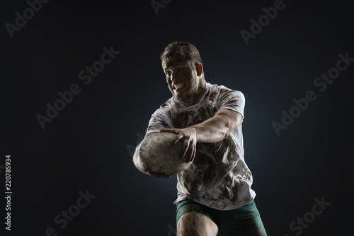 Isolated dirty rugby player with rugby ball on dark background © Alex