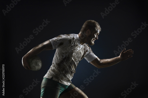 Isolated dirty rugby player with rugby ball on dark background © Alex