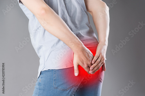 Man suffering from hemorrhoids, anal pain on gray background