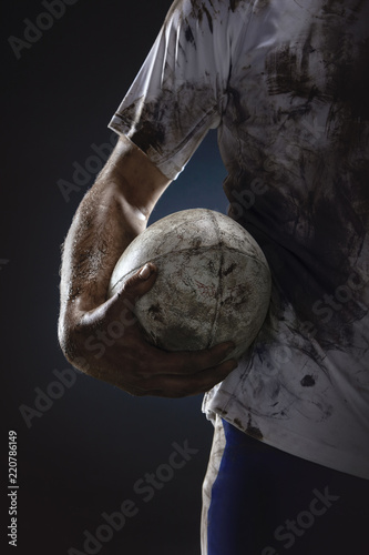 Rugby player hands with ball on dark background. Close up photo