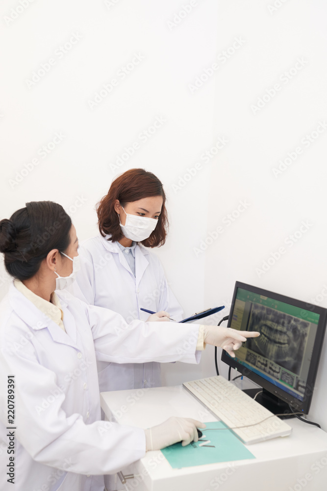 Asian female dentists in office looking at computer screen with panoramic dental x-ray and having discussion Asian female dentists in office looking at computer screen with panoramic dental x-ray and having discussion