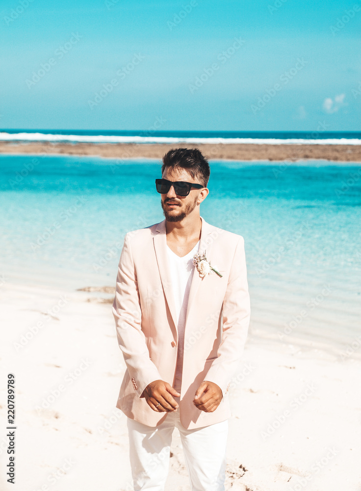 Portrait of handsome bridegroom in pink suit posing on the beach behind blue sky and ocean Portrait of handsome bridegroom in pink suit posing on the beach behind blue sky and ocean