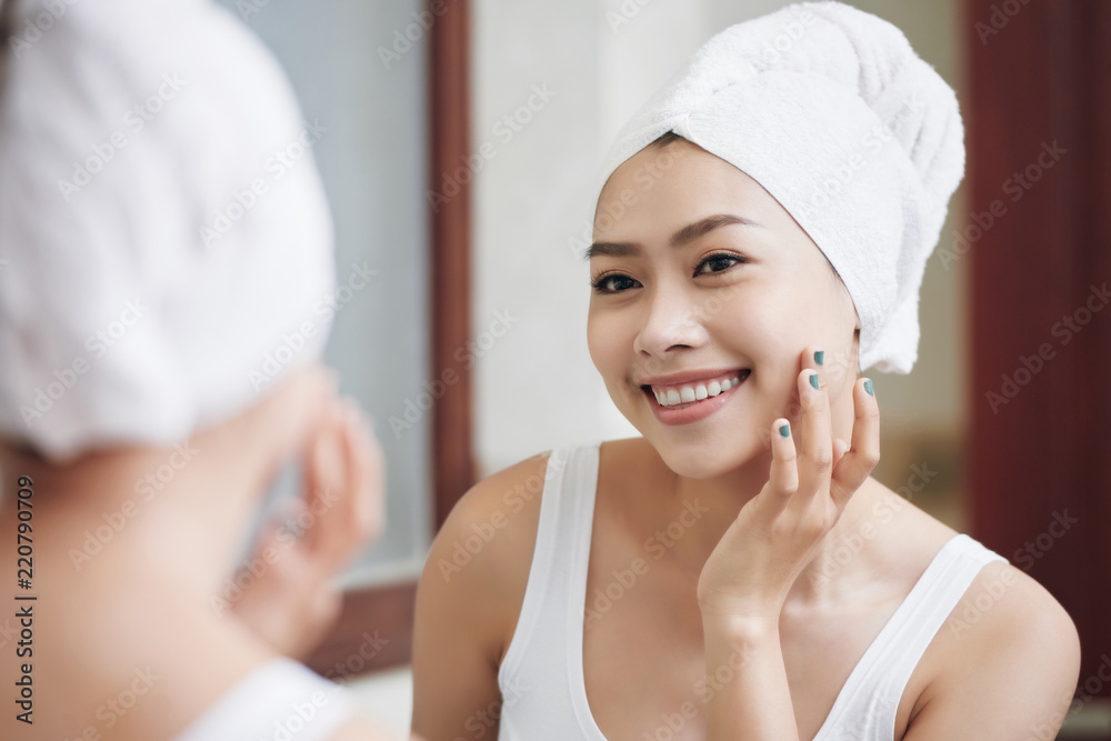 Charming Asian woman in white towel touching pure and soft skin looking in mirror reflection Charming Asian woman in white towel touching pure and soft skin looking in mirror reflection