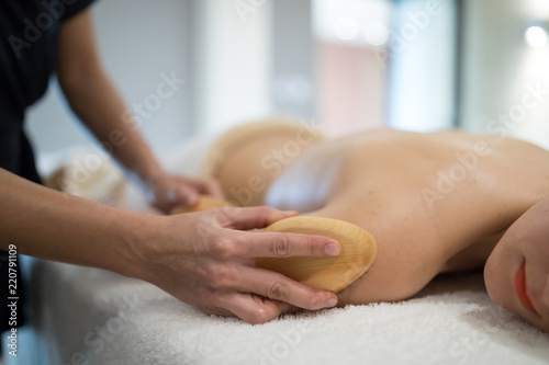 Massage therapist using wooden tool to massage patient