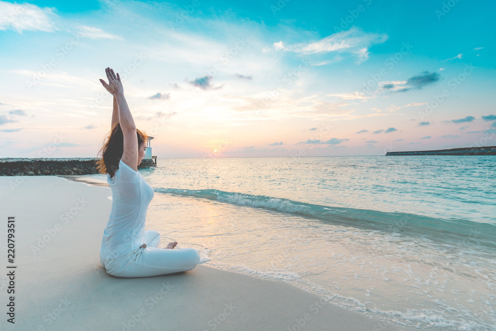 Asian woman wearing white sportswear practicing yoga Lotus pose to meditation on the beach in Maldives at sunset,Feeling so comfortable and relax in holiday,Healthy Concept