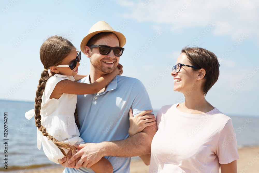 Waist up portrait of happy modern family smiling and embracing lovingly while walking along beach enjoying Summer vacation