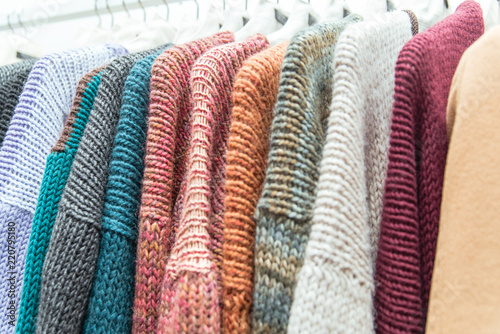 Nice warm colorful sweaters hang on hangers inside of a shopping mall. Beautiful clothes for winter autumn season. Wool things for fall. Classic design. Merchandise in a shop © Julia