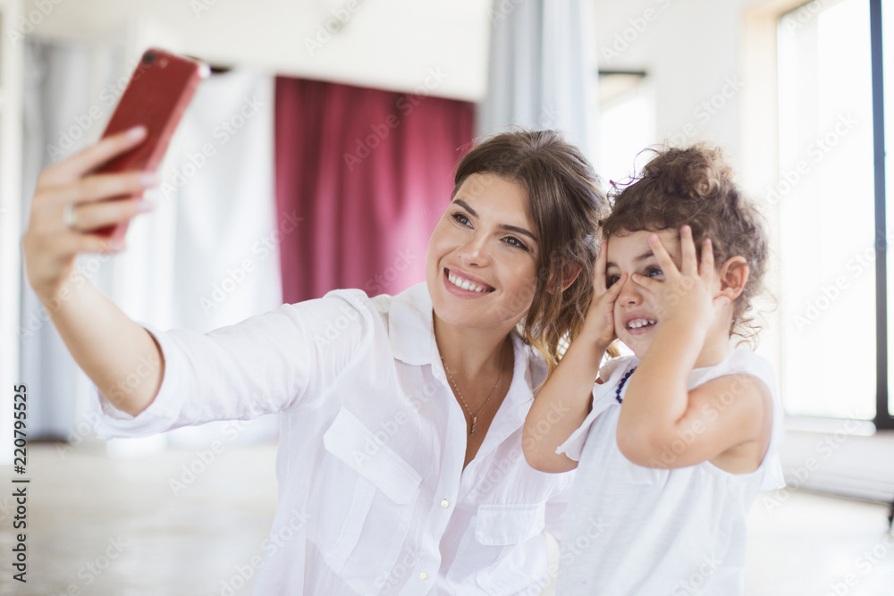 Pretty smiling mother and cute little daughter happily taking ph