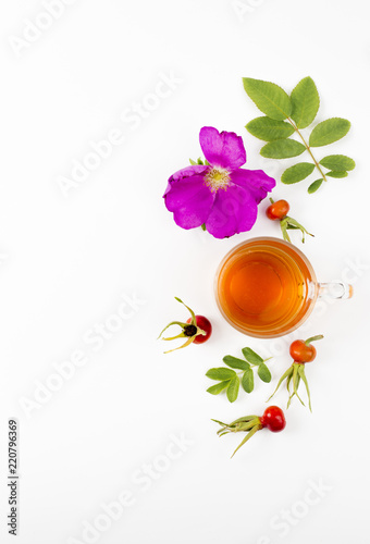 Flat lay view of the rose hip or rosehip, also called rose haw and rose hep tea in clear glass cup, raw berries, blossom and leaves for decoration on white background. Minimal composition.