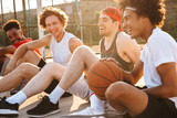 Young happy basketball players sitting at playground outdoor, and watching game during summer sunny day