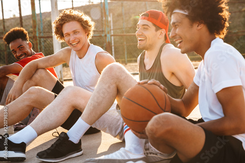 Young happy basketball players sitting at playground outdoor, and watching game during summer sunny day photo