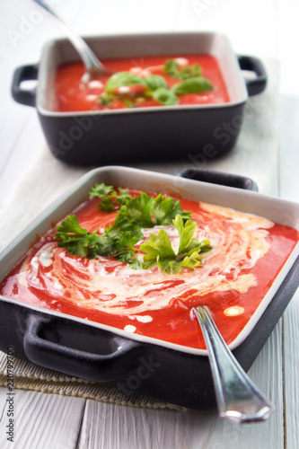 Creamy tomato soup in bowls with spoons on white wooden surface , vertical