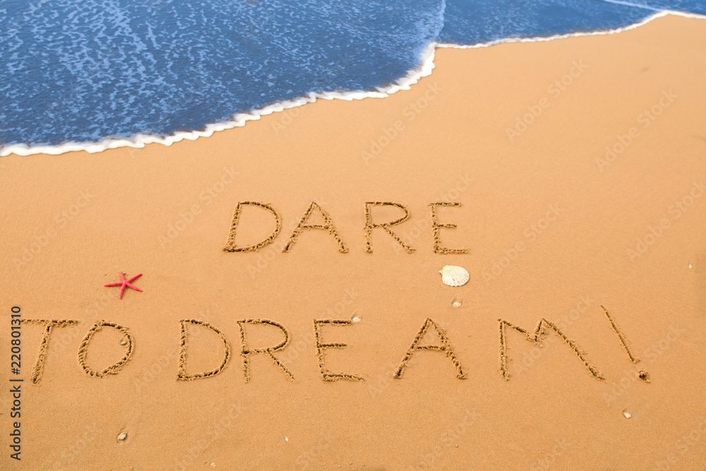 dare to dream written in the sand on a sunny beach