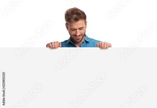 smiling casual man holding blank board looks down at it