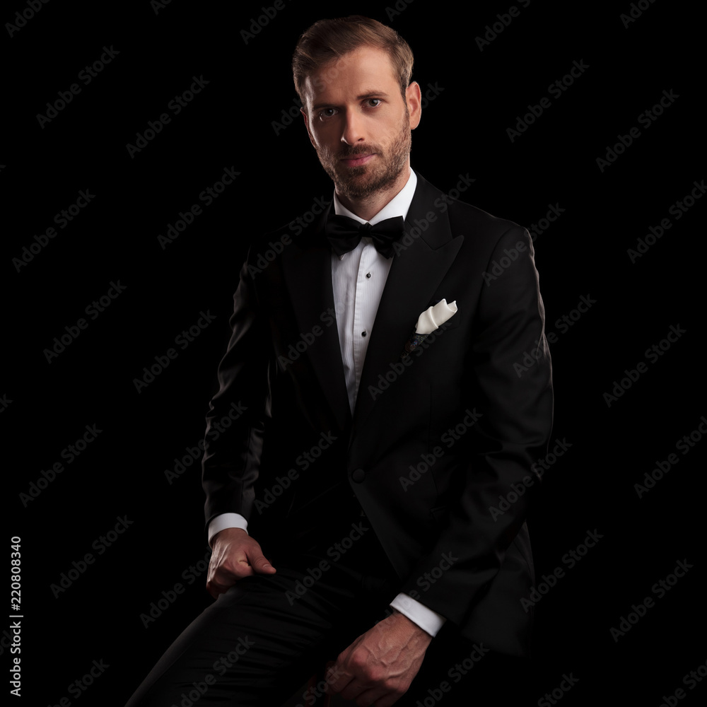 young elegant man in tuxedo resting on a chair