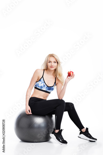 Fit young pretty woman sitting on the fitness ball with apple in hand. Health concept.