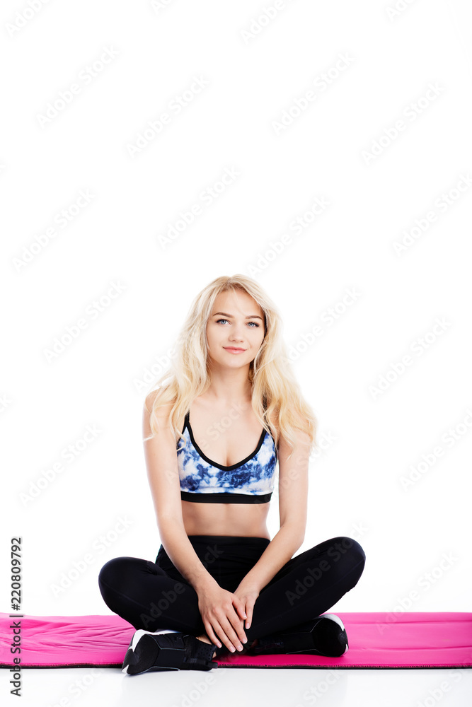 Fit young pretty woman sitting on the pink fitness mat.