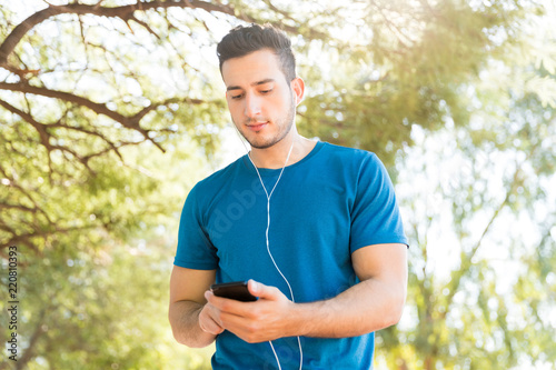 Fototapeta Naklejka Na Ścianę i Meble -  Jogger Listening Music With Earphones And Mobile Phone In Park