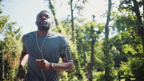 Happy african american man run listen music in headphones using the phone smile at park smartphone training active athlete body exercise fit health sport workout runner summer app muscular jogging