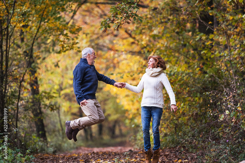 Senior couple in an autumn nature, holding hands and jumping.