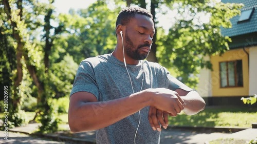 african american man run listen music in headphones using smartwatch smile at park sunshine training active athlete body exercise fit health sport workout runner summer app muscular jogging