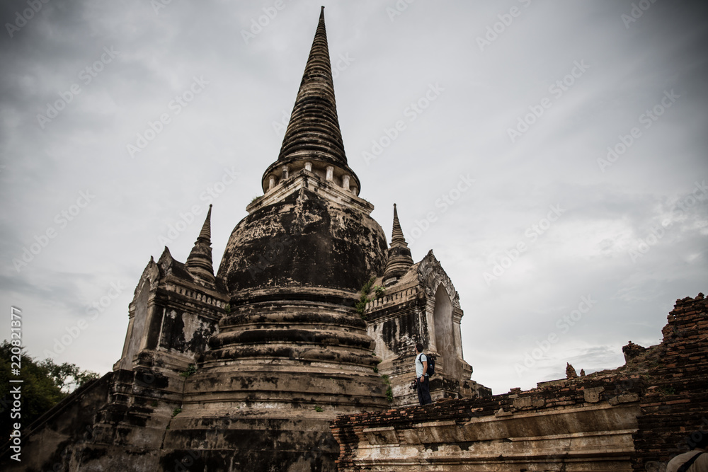 Obraz premium A western traveler boy observes the ruins of the temples in the old capital of Ayutthaya in the background of a storm coming