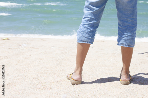 Behind the black of legs woman wearing jeans on beautiful sandy beach tropical sea.