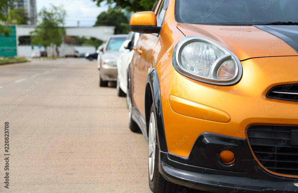 Closeup of front side view of orange car parking beside the street in sunny day. 