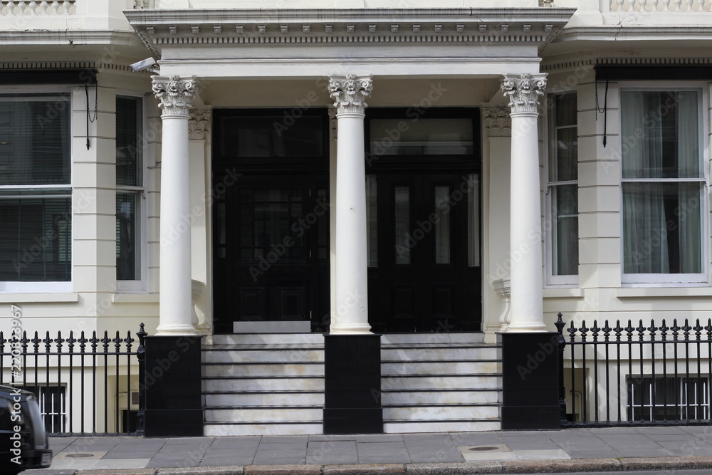 Entrance of a private London building with three white columns and a flight of stairs leading to the black doors creating a strong contrast