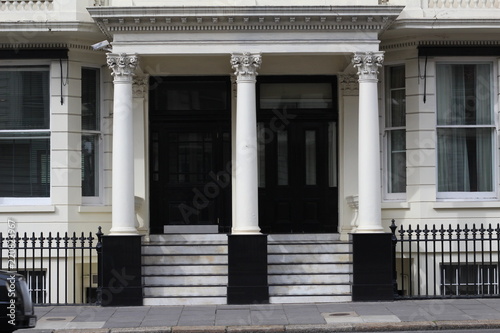 Entrance of a private London building with three white columns and a flight of stairs leading to the black doors creating a strong contrast © NibaPhoto