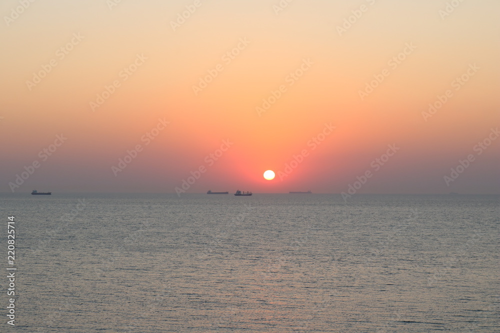 Sunset with container ships waiting on their turn to cross through Gallipoli seen from the island Bozcaada in Turkey.